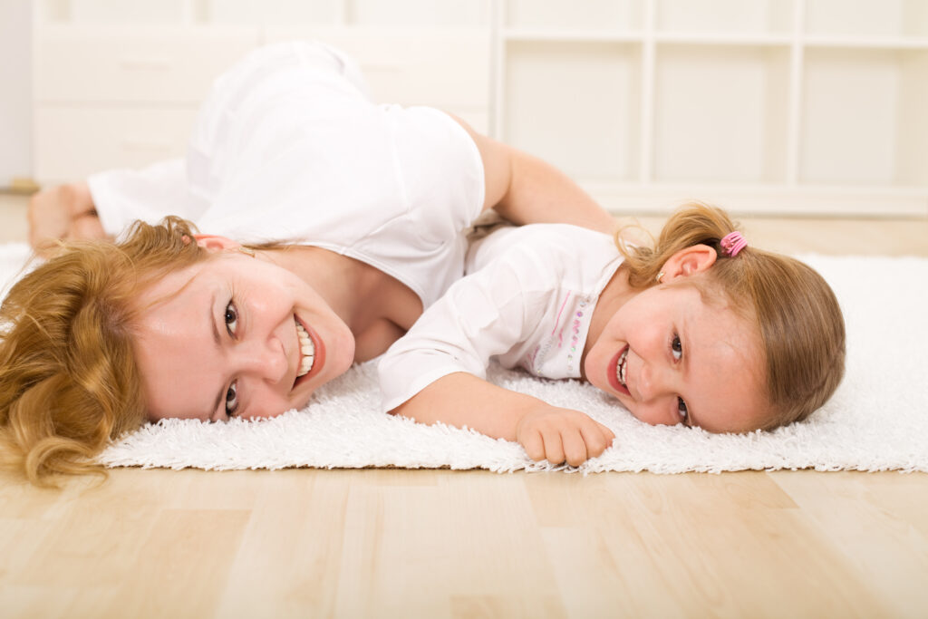 a photo of a mother and daughter staring at the camera with smiling faces while laying on a white furry looking rug