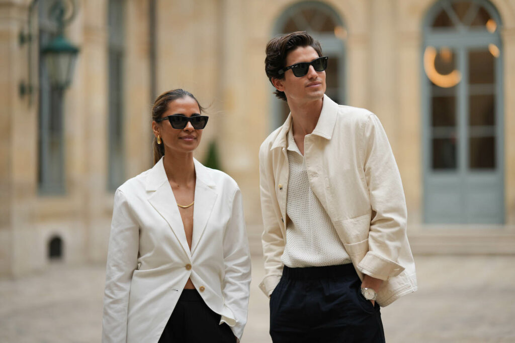 Photo of a male and female dressed in white blazers and wearing sunglasses.