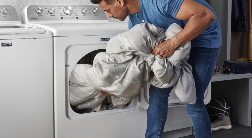 Photo of male putting bedding into a residential mashing machine.