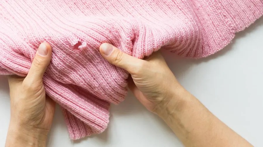 Photo of hands holding a pink sweater with a tear in the seam