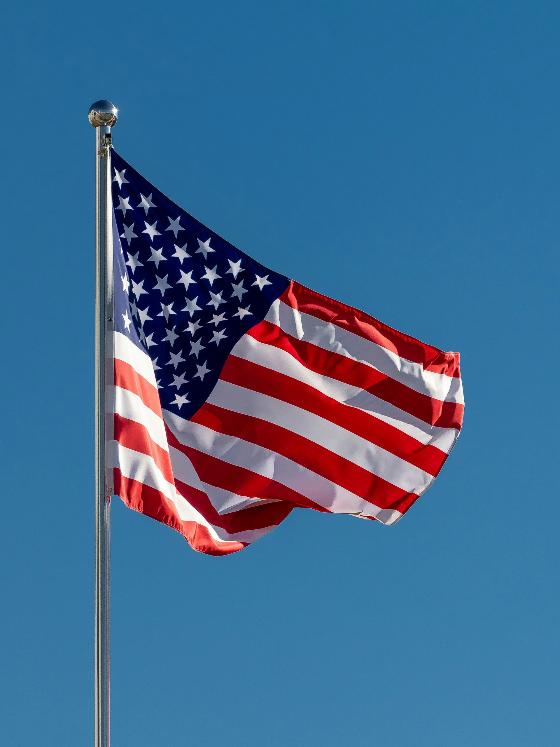 The United States flag waves on a flagpole against a clear blue sky.