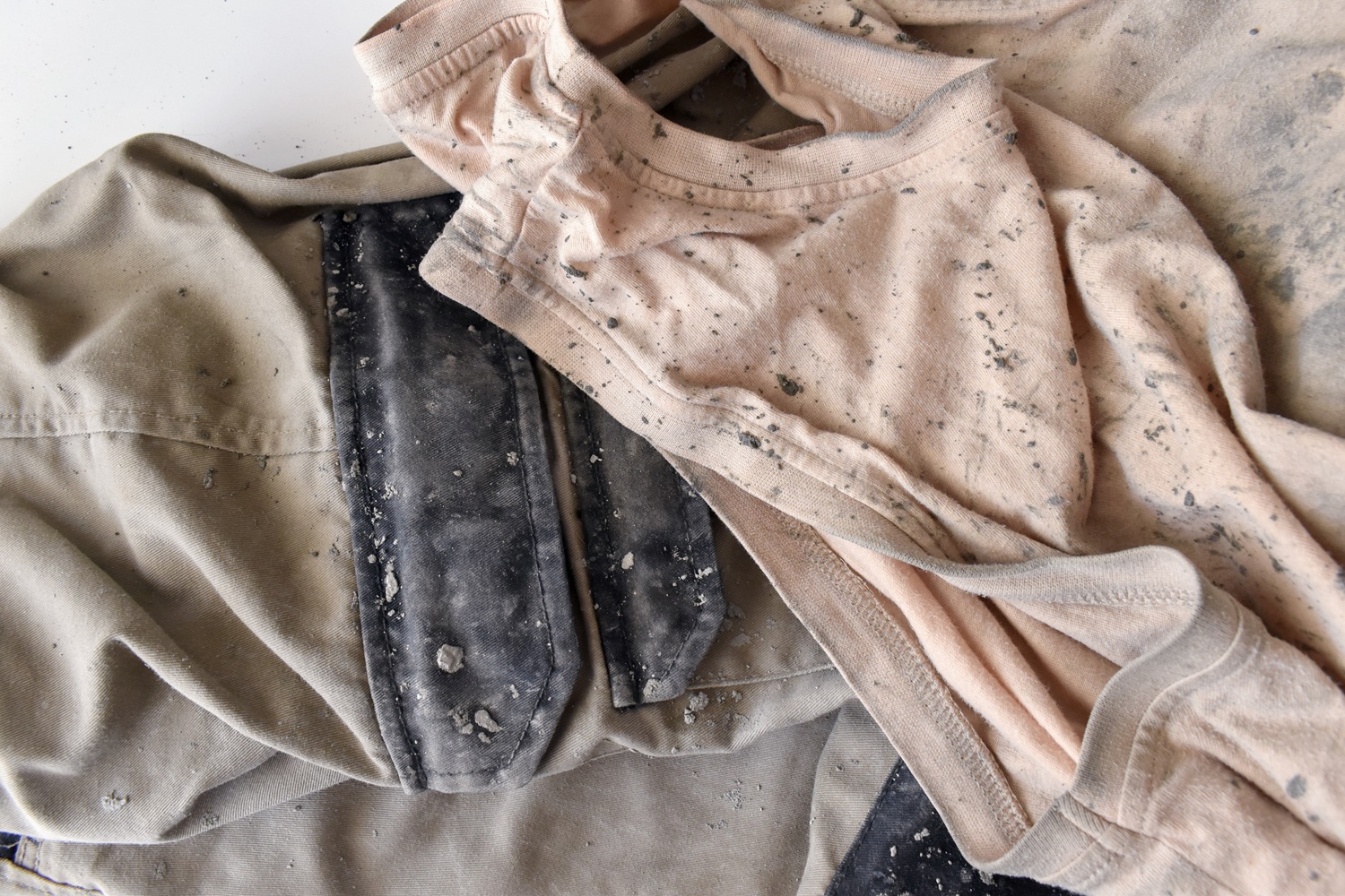 Two pieces of clothing, one gray and one light pink, are covered in spots of dust and dirt.