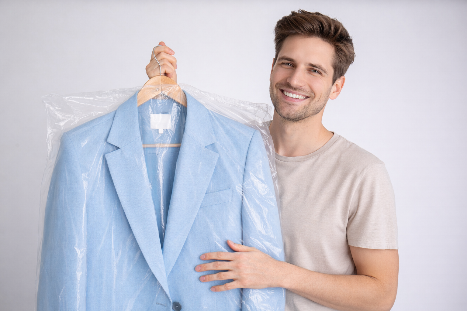 Smiling person holding a light blue suit jacket on a hanger, covered in clear plastic garment bag.