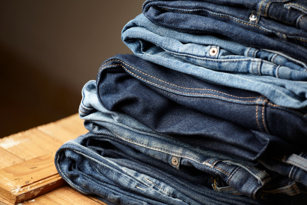 A stack of folded blue jeans in varying shades sits on a wooden surface. A stack of folded blue jeans in varying shades sits on a wooden surface.
